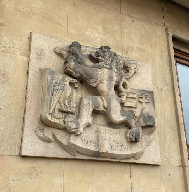 Pamětní deska k podpisu Olomoucké smlouvy. Havran, který drží prsten je erb Matyáše Korvína, vpravo vidíme erb Vladislava Jagellonského. Mezi erby vidíme lva, znak Čech. Autor desky - Vojtěch Hořínek